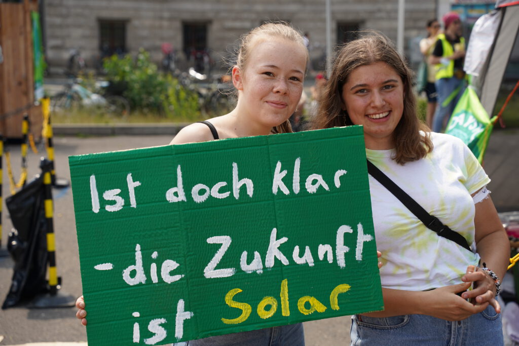 Zwei Personen halten ein Schild mit "Ist doch klar - die Zukunft ist solar".
