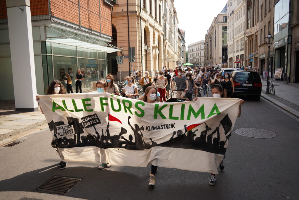 Menschen laufen in einer Demonstration durch die Leipziger Innenstadt. Im Vordergrund laufen mehrere Personen mit einem Fridays for Future Banner.