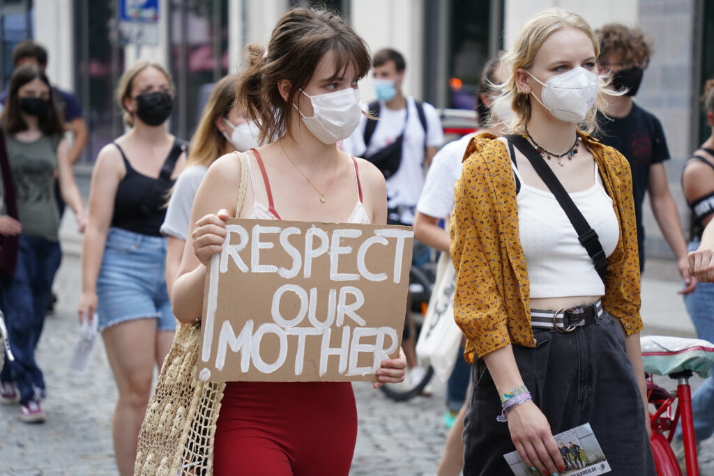 Zwei Personen laufen auf einer Demonstration. Die linke Person hält ein Schild, auf dem "Respect our Mother" steht.
