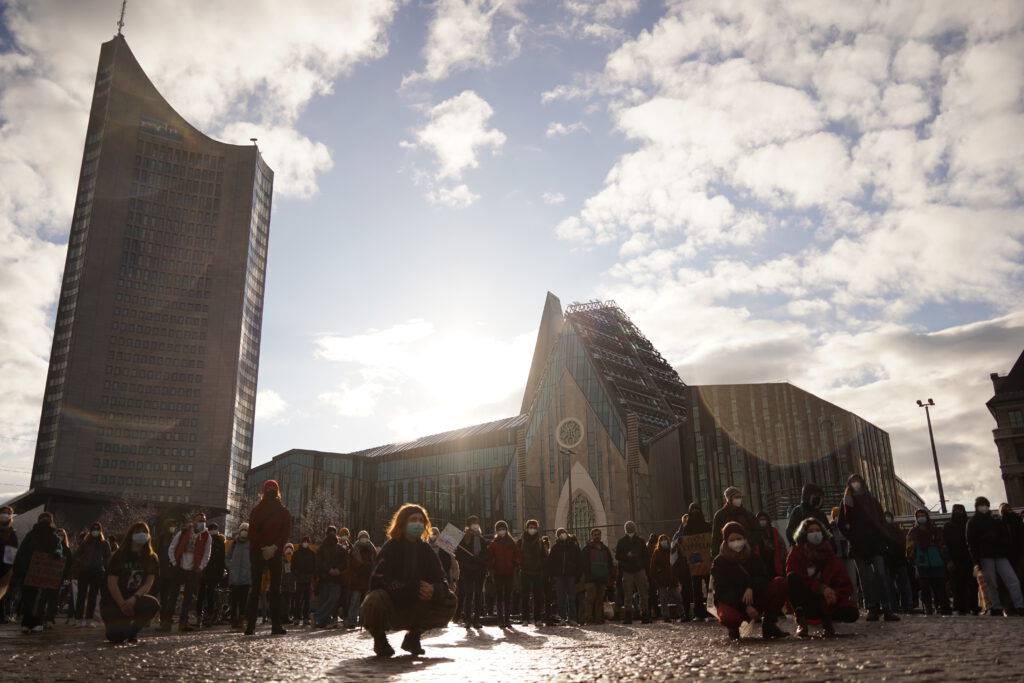 Ca. hundert Personen stehen auf dem Augustusplatz in der Sonne und hören einem Redebeitrag zu.